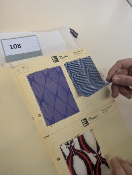 Een hand tilt een textielstaal in een boek op